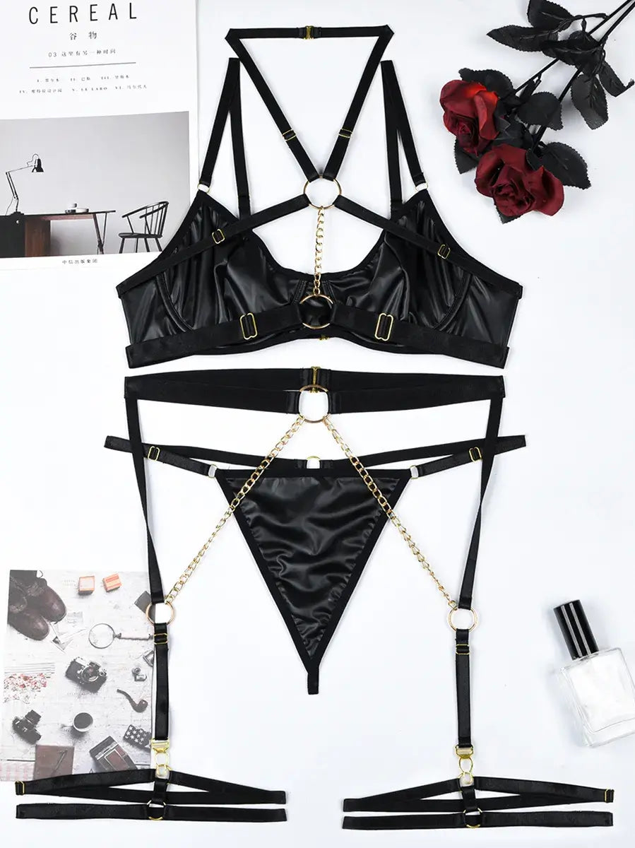 Flat lay display of black PU leather neckpiece and gold chain accessories included in the Obsidian Edge lingerie set.