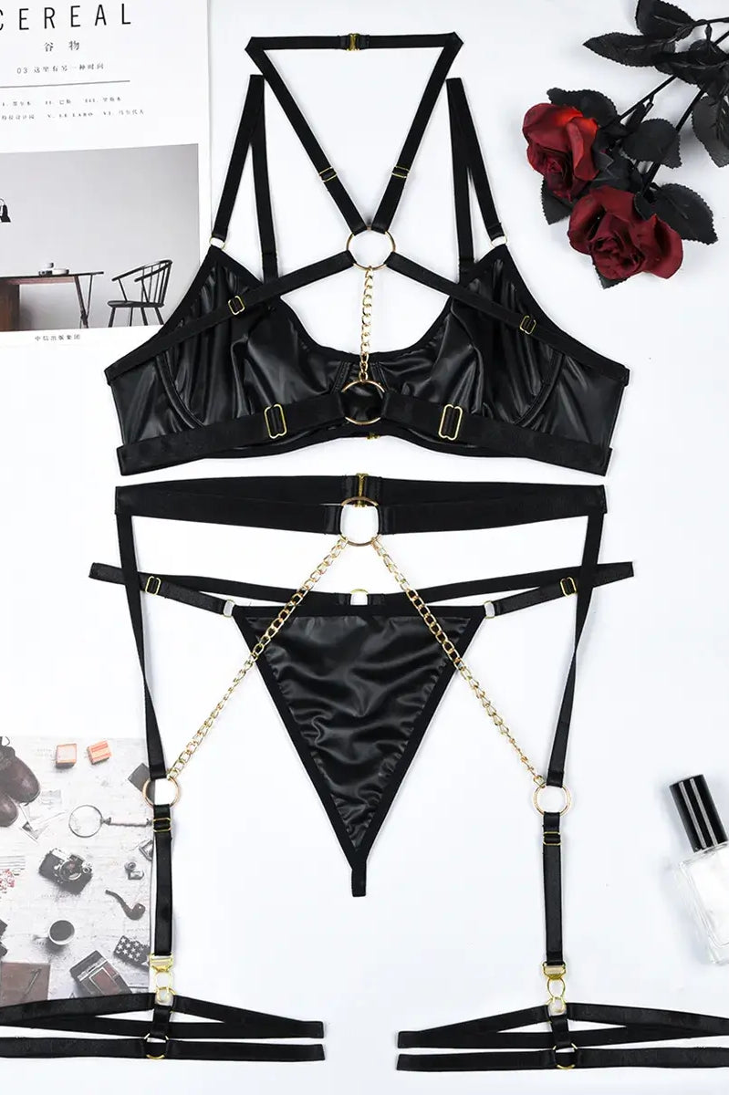 Flat lay display of black PU leather neckpiece and gold chain accessories included in the Obsidian Edge lingerie set.